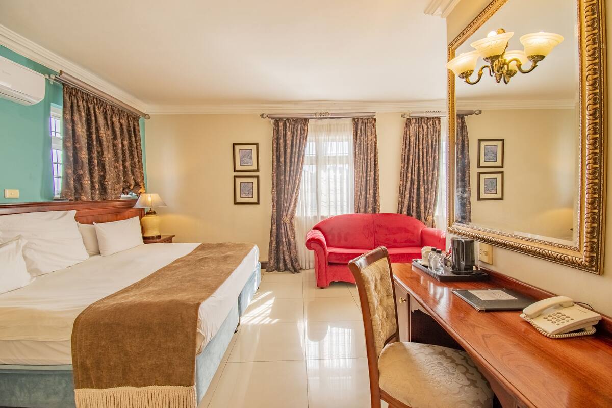 Habitación de hotel con cama, escritorio con teléfono, silla, sofá rojo y espejo grande.