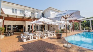 Un espace aménagé au bord de la piscine, avec des parasols blancs et des sièges, une piscine à l’eau d’un bleu limpide et un bâtiment doté de balcons.