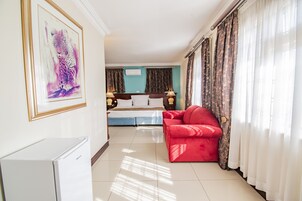 Quarto de hotel com uma cama, um sofá vermelho, um refrigerador branco e um quadro na parede.