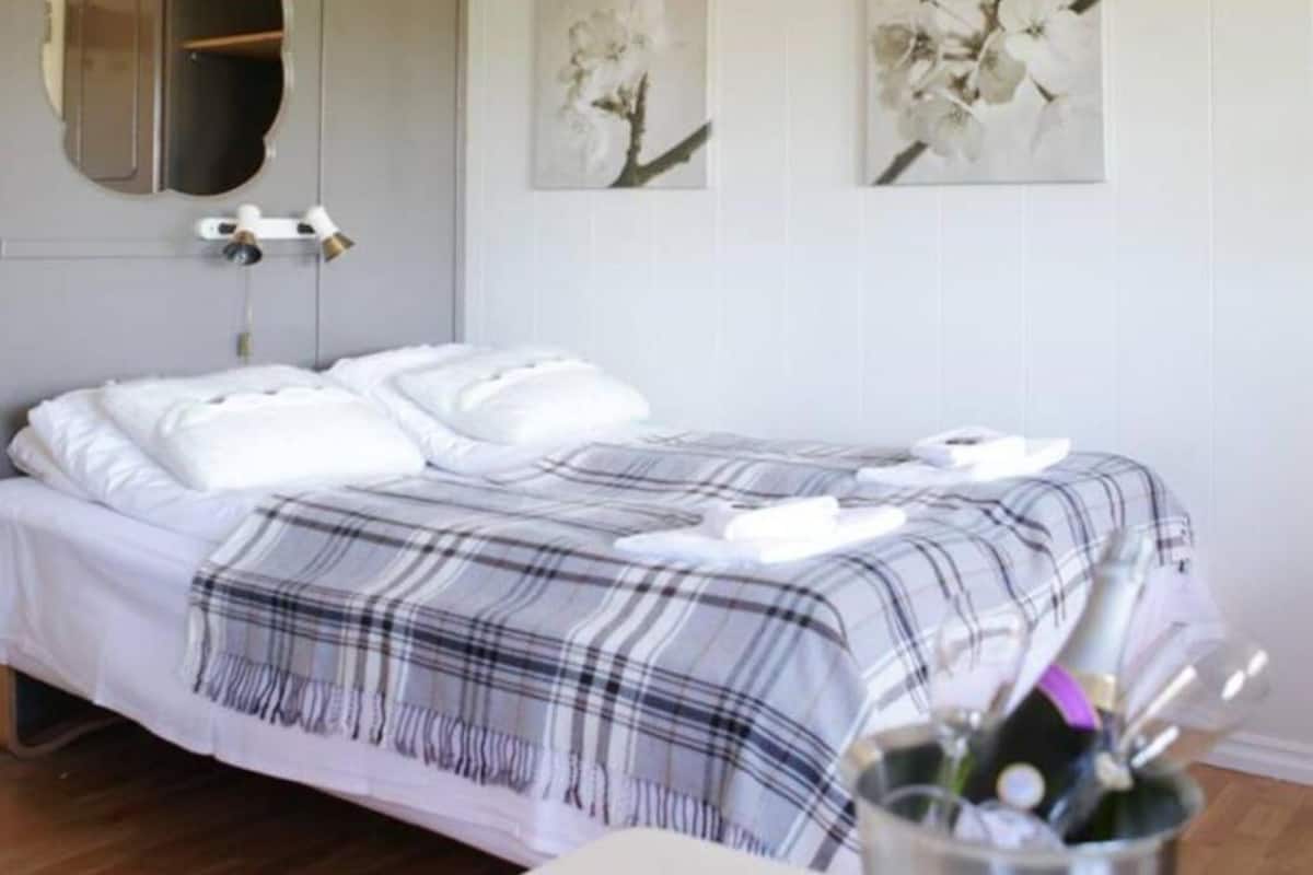 A neatly made bed with a plaid blanket, a bedside table with a cup holder, and two wall-mounted paintings of flowers.