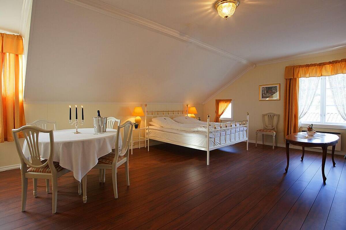 A bedroom with a bed, a table with chairs, a small round table, and a window with curtains.