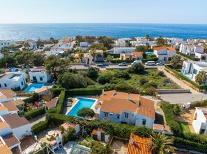 Un quartier résidentiel situé sur la côte, avec des bâtiments blancs, une piscine et une vue sur la mer.