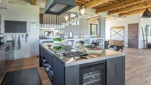A modern kitchen with a central island, wooden beams, and a large window. - Casale The Place 6+2, Emma Villas (San Damiano)
