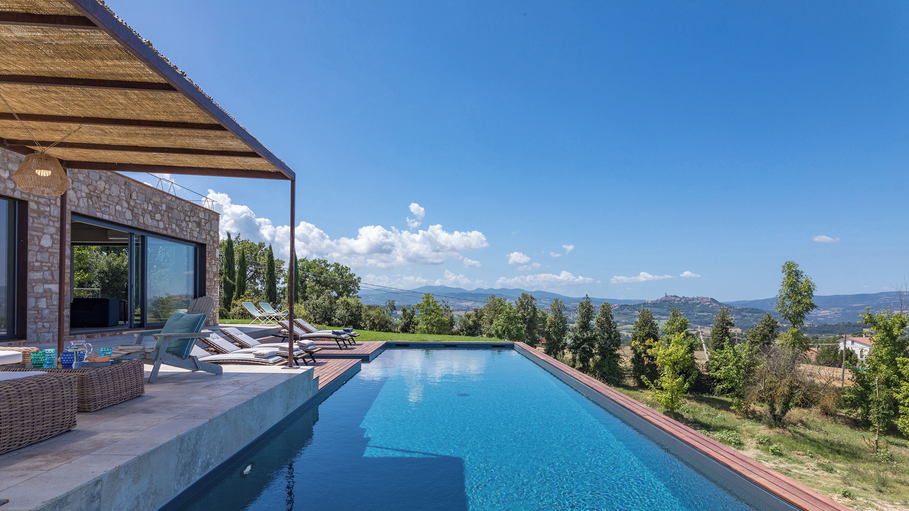 A modern house with a swimming pool, stone walls, and a view of the mountains.