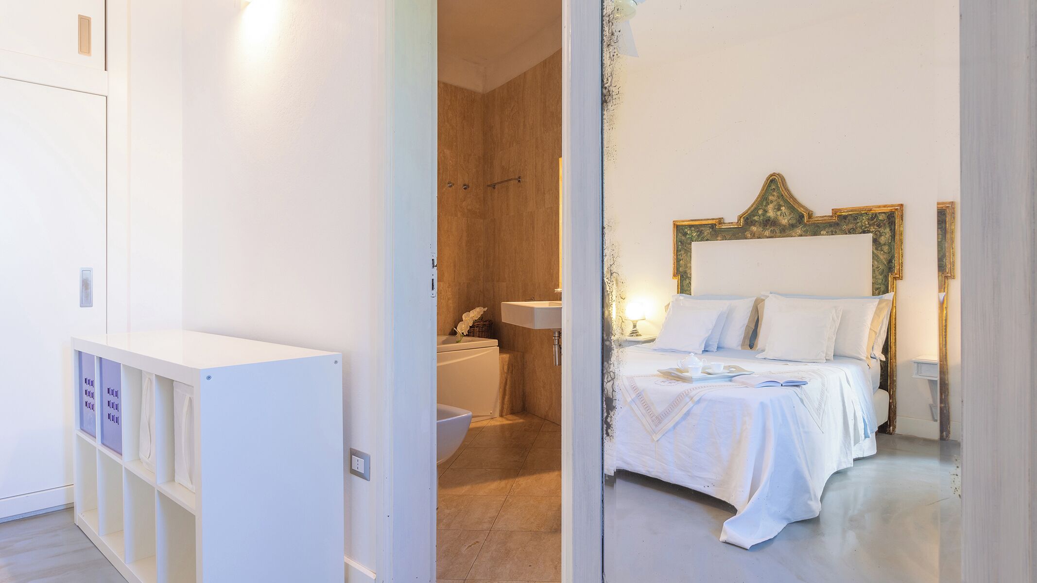 Une chambre d’hôtel comprenant un lit, une table de chevet, une commode, une salle de bain avec un lavabo et des toilettes, et une armoire.