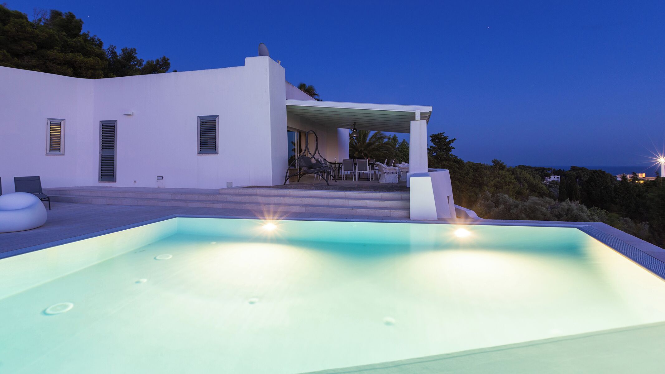 A modern house with a swimming pool, outdoor seating, and a view of the sea.