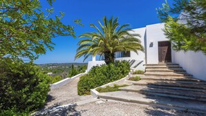 A white building with a stone staircase leading to a wooden door, surrounded by greenery and a clear blue sky. - Villa Calypso 8, Emma Villas (Castrignano del capo)