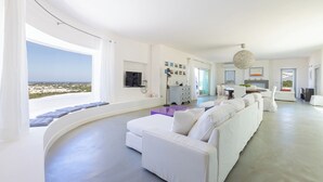 A modern living room with a white sofa, a purple ottoman, and a view of the sea. - Villa Calypso 8, Emma Villas (Castrignano del capo)