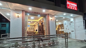 L’entrée d’un hôtel, avec un panneau indicateur, un espace extérieur couvert aménagé en coin salon et une entrée fermée par un portail.