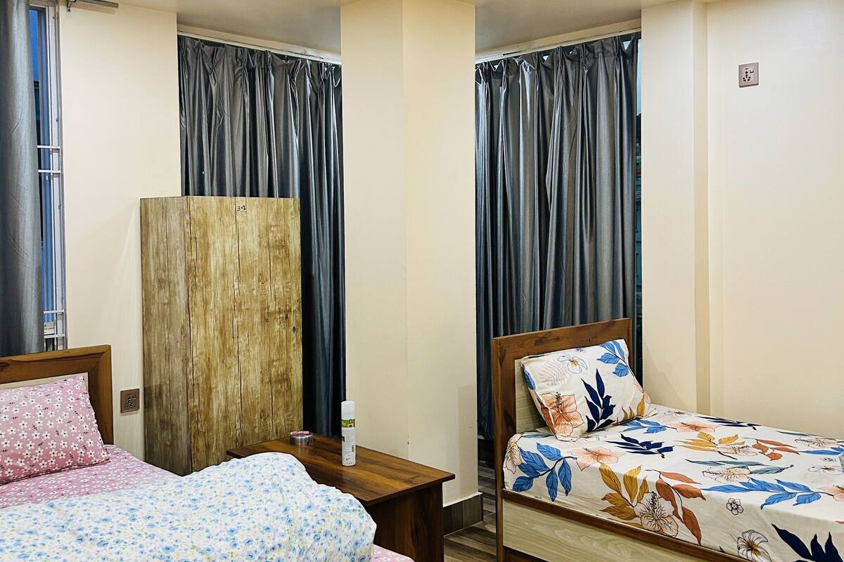 A hotel room with two beds, wooden headboards, a nightstand, a wooden wardrobe, and a window with curtains.