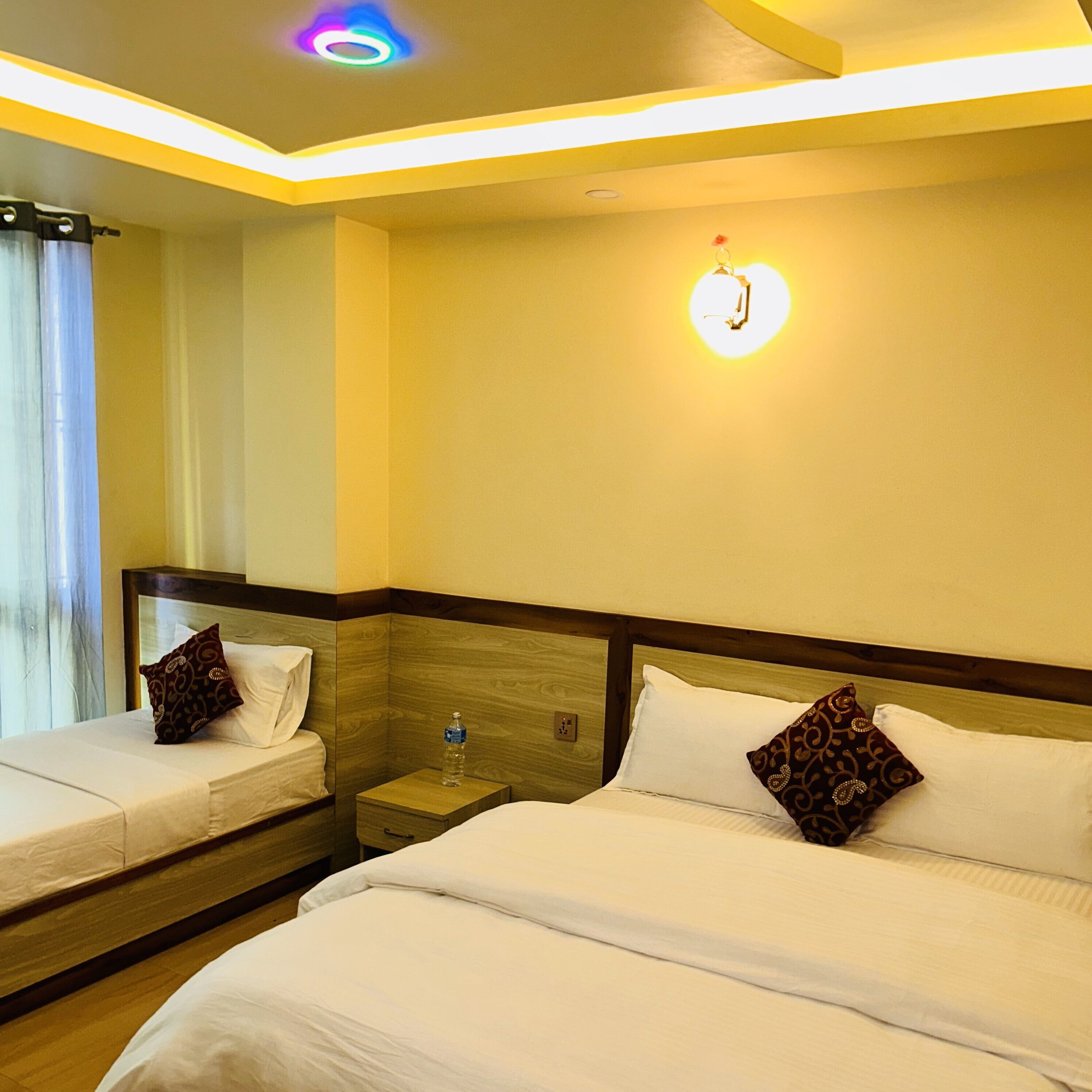 A hotel room with two beds, a nightstand, a wall-mounted light, and a ceiling light.