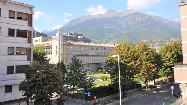 A building with a modern architectural style, surrounded by trees and a mountain in the background. - Casa Alpina - Aosta (Aosta)