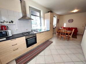 A modern kitchen with a gas stove, oven, and microwave. There is a dining area with a table and chairs, and a red sofa in the background. - Casa Alpina - Aosta (Aosta)