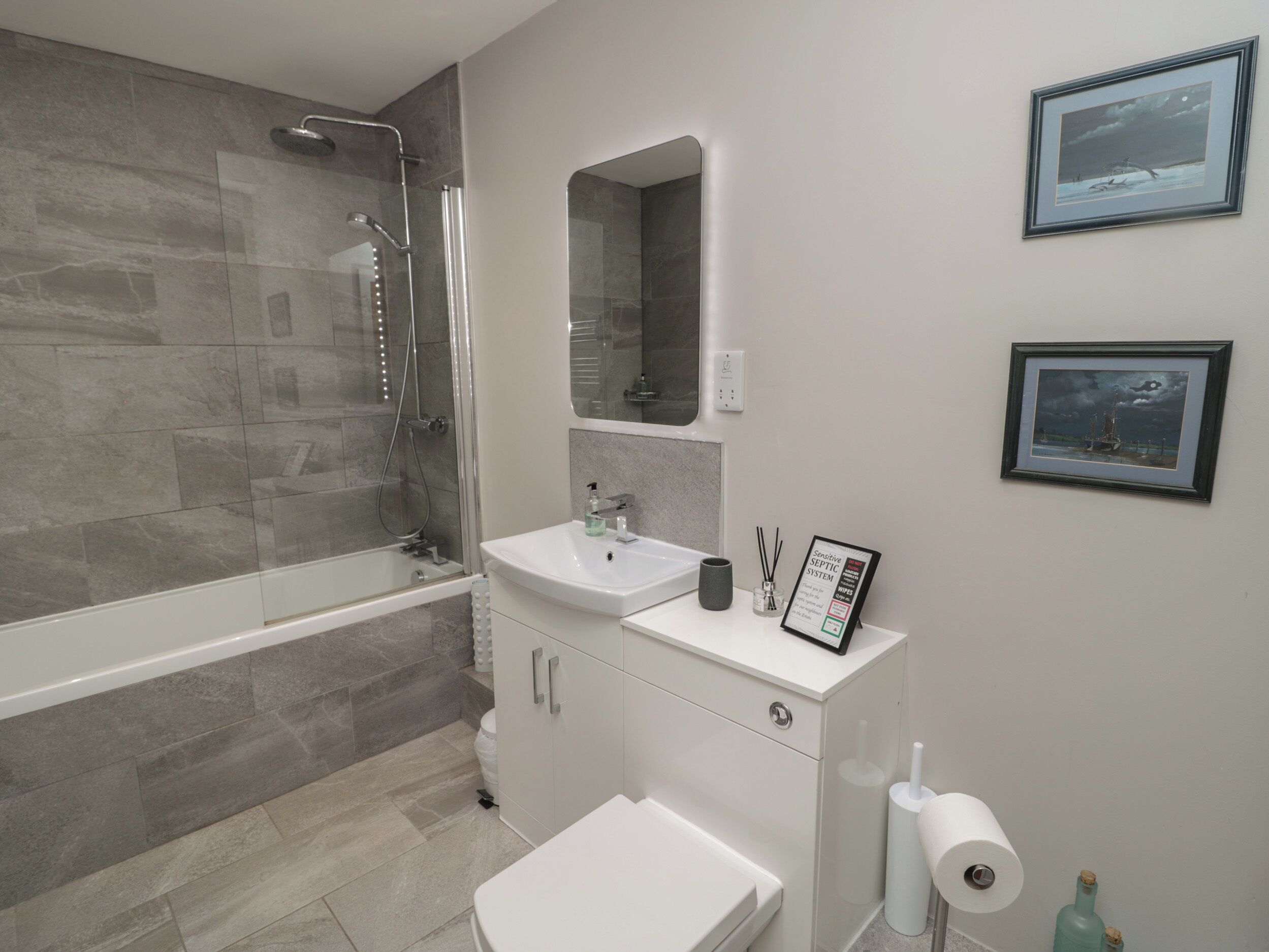 A modern bathroom with a glass-enclosed shower, a white sink, and a toilet. There are framed pictures on the wall.