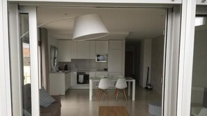Una cuina moderna amb armaris blancs, microones i zona de menjador amb dues cadires blanques.