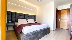 A modern bedroom with a large bed, a dark headboard, and a bedside table. - Şirin Rezidence (Denizli)