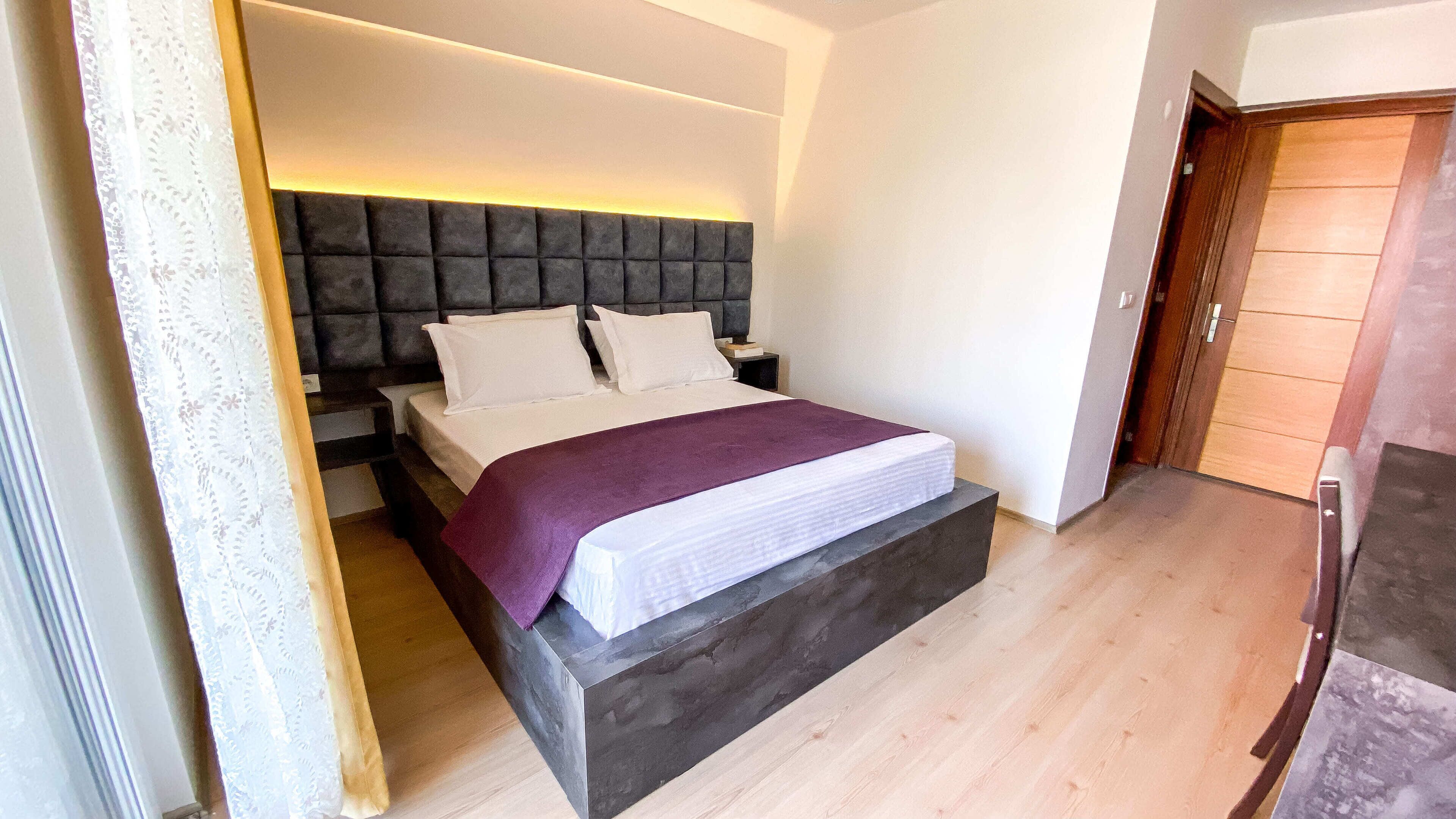 A modern bedroom with a large bed, a dark headboard, and a wooden floor.