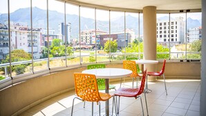 A balcony with a round table and chairs, large windows with a cityscape view, and a tiled floor. - Şirin Rezidence (Denizli)