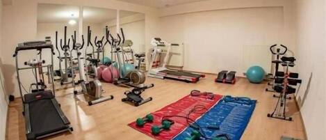 Un gimnasio en casa con diverso equipo de ejercicio, incluyendo cintas de correr, bicicletas estáticas y pesas libres.