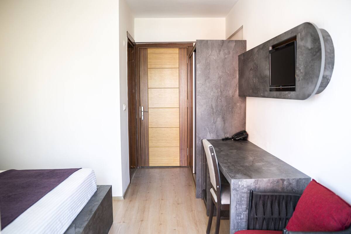 A compact room with a wooden door, a built-in TV, a small table, and a chair.