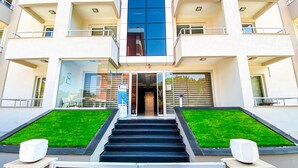 A modern building with a glass entrance, a staircase leading up, and a small green lawn area. - Şirin Rezidence (Denizli)