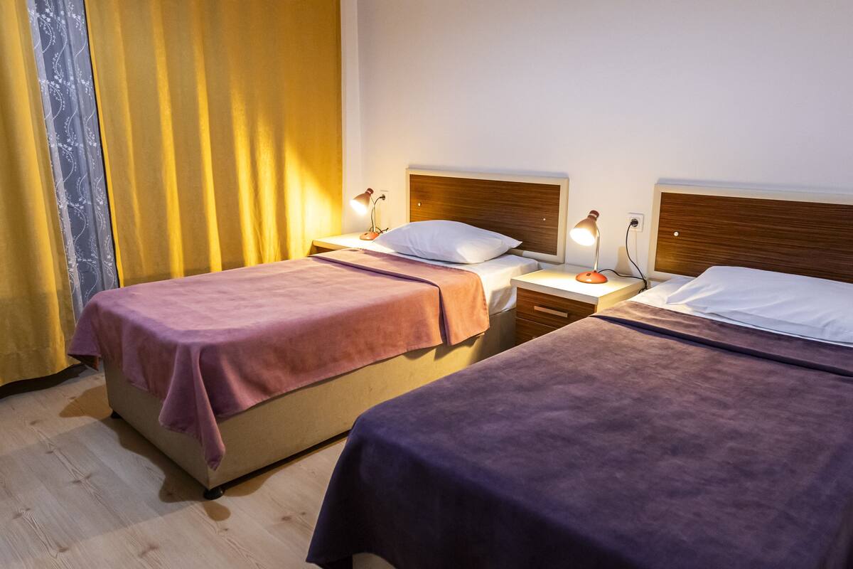 A hotel room with two beds, each with a wooden headboard, a bedside table, and a lamp.