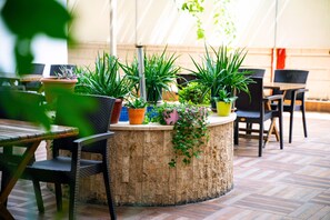 A wooden table surrounded by chairs, with potted plants on a circular wooden stand. - Şirin Rezidence (Denizli)