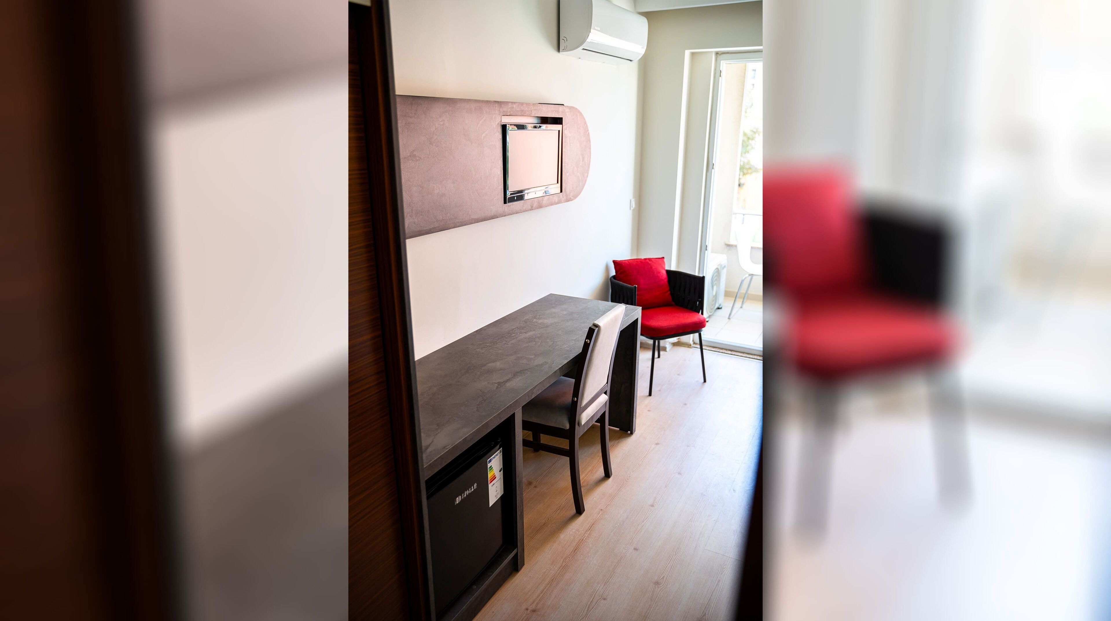 Een moderne kamer met een donker houten bureau, een rode stoel en een groot raam.
