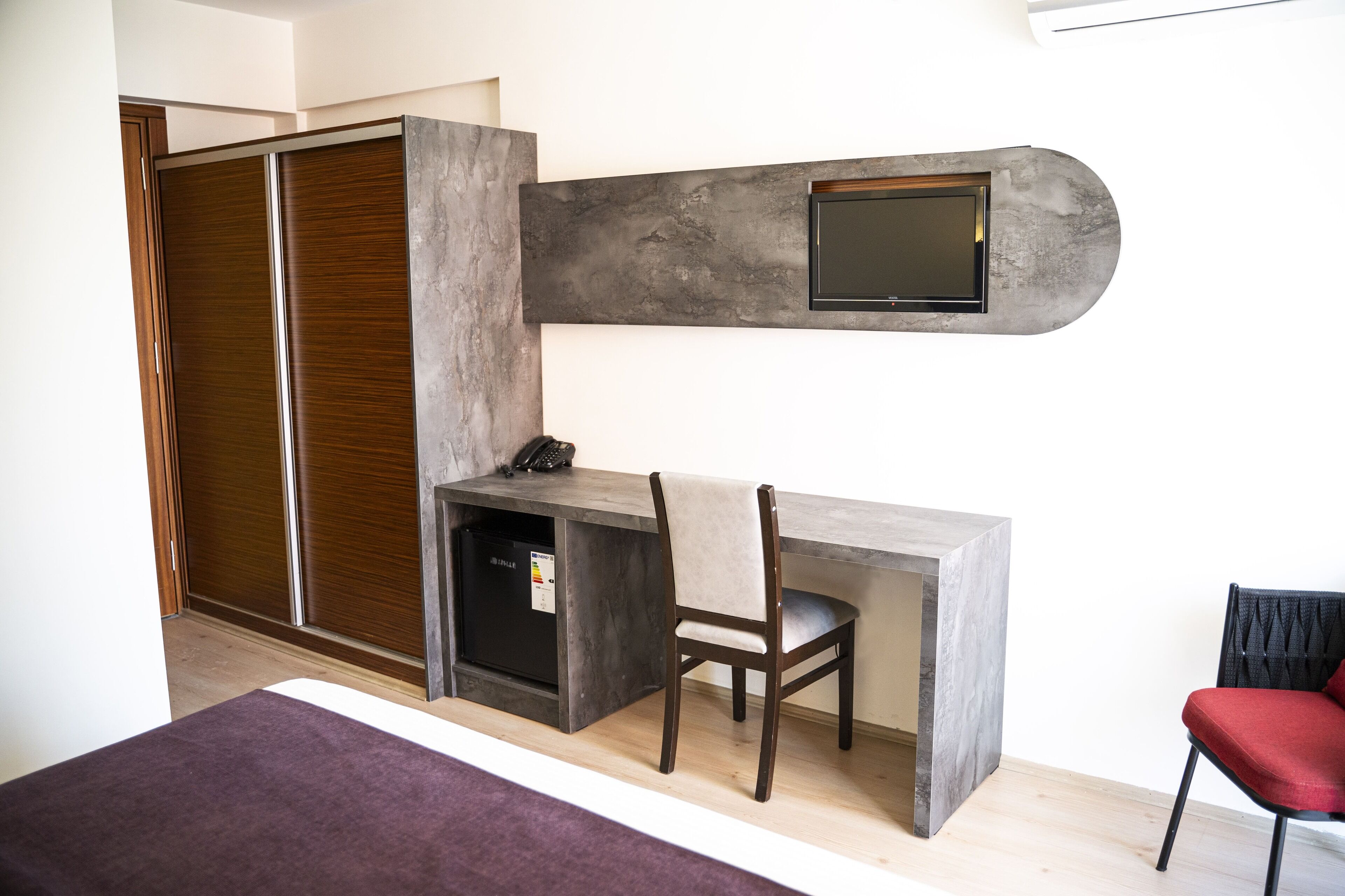 A compact bedroom with a built-in desk, a wardrobe, and a TV mounted on the wall.