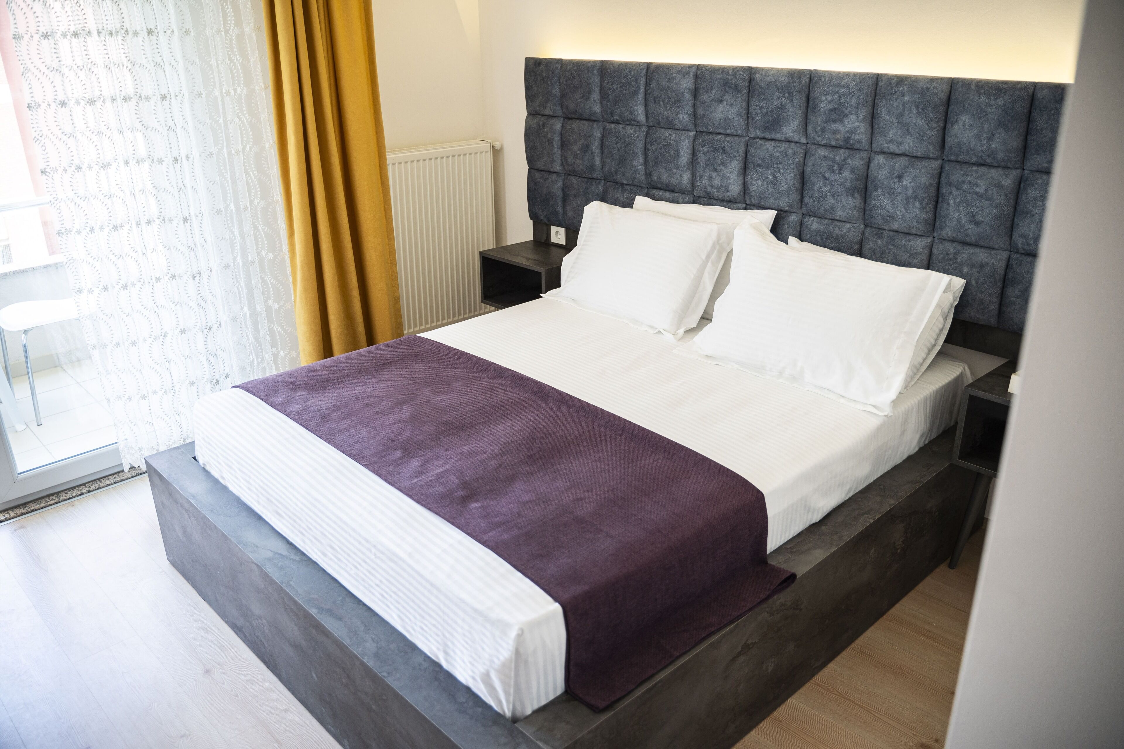 A modern bedroom with a large bed, a headboard, and a nightstand.
