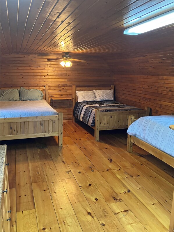 A cabin with three wooden beds, a ceiling fan, and a skylight.