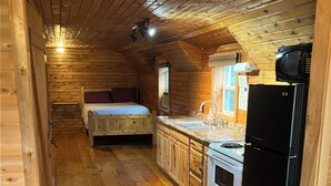Una cabaña compacta con interior de madera, una kitchenette, una cama y una pequeña zona de estar.