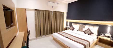 A hotel room with a bed, a desk, a chair, a TV, and a ceiling fan.