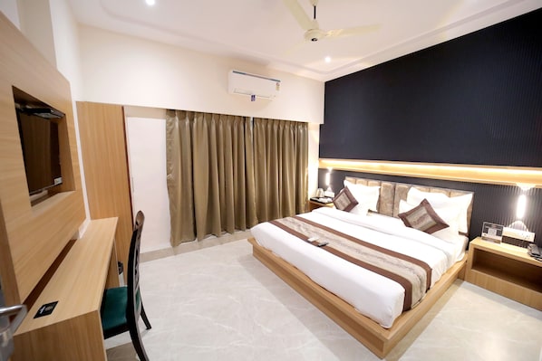 A hotel room with a bed, a desk, a chair, a TV, and a ceiling fan. - HOTEL ALFA EXECUTIVE (Mumbai)