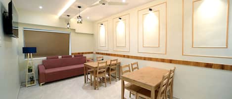 A modern living room with a sofa, a dining table with chairs, a ceiling fan, and wall-mounted lights.