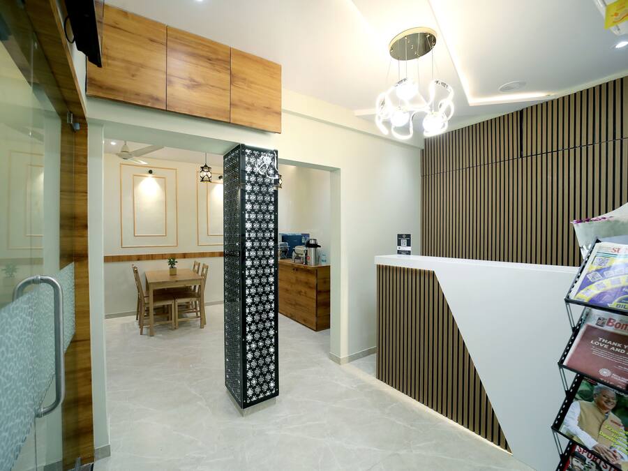 Un interior moderno con techo de madera, una columna central con diseño decorativo, una zona de comedor con mesa y sillas de madera, y un mostrador de recepción con revistas.