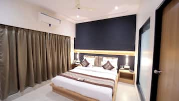 A hotel room with a bed, bedside tables, a ceiling fan, an air conditioning unit, and a door.