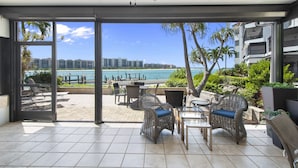 A spacious outdoor patio with wicker furniture, a ceiling fan, and a view of the ocean and buildings in the background. - Special Savings January 2024 31 days minimum! (Naples)