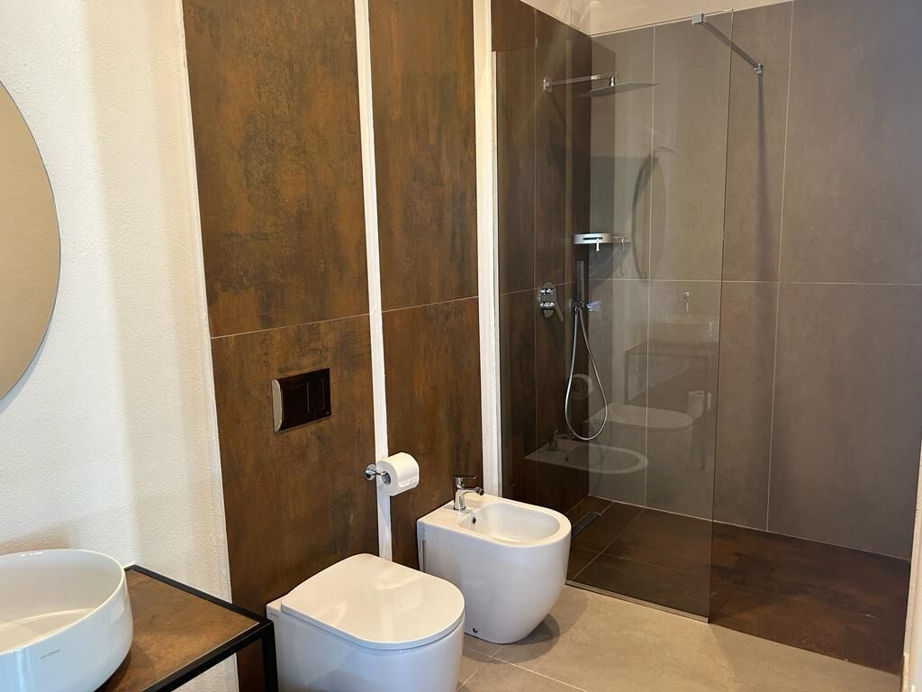 A modern bathroom with a bidet, a toilet, and a shower area.