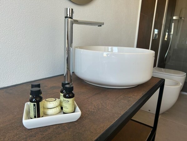 Casa de banho com lavatório branco, torneira moderna e um pequeno prato com produtos de higiene pessoal.