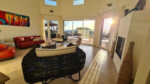 A spacious living room with a red sofa, a black wicker chair, and a dining area with a table and chairs. - Casa El Mirador Offers Spectacular Views, Comfort, and a Heated Pool (arenas)