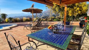 An outdoor patio with a tiled table, chairs, a grill, and a pool.