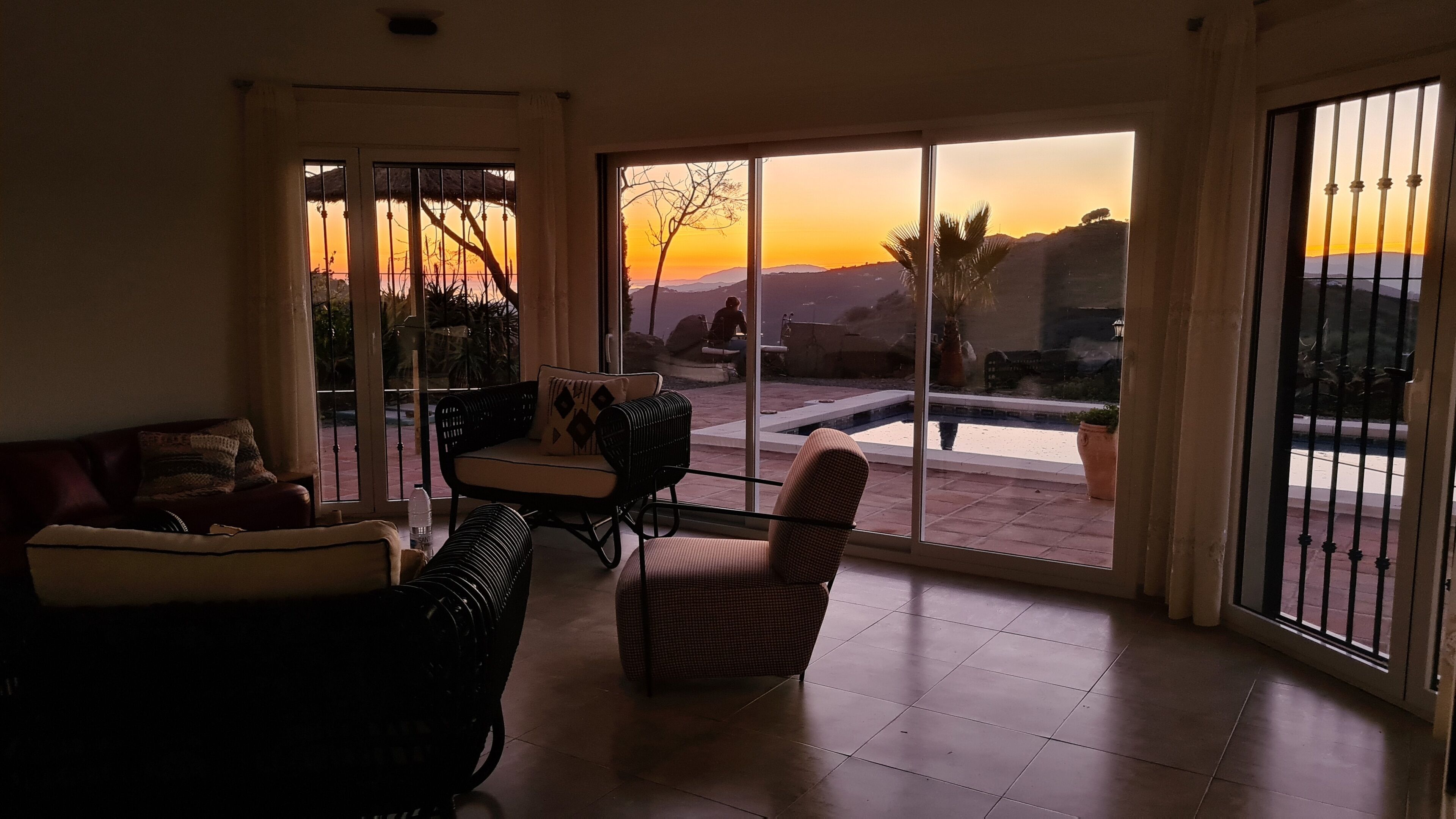 A spacious living area with a large sliding glass door leading to a patio. Inside, there is a sofa, a chair, and a small table.
