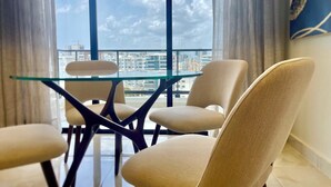 A modern room with a glass table and chairs, large windows with a city view, and a balcony. - Luxury in Naco 2BR: Pools, gym, views, bars and more (Santo Domingo)