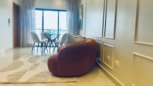 A modern living room with a large window, a dining area with chairs, and a red bean bag chair. - Luxury in Naco 2BR: Pools, gym, views, bars and more (Santo Domingo)