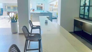 A modern living room with a dining area, a TV, and a view of a pool and balcony. - Luxury in Naco 2BR: Pools, gym, views, bars and more (Santo Domingo)