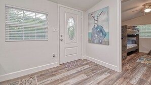 Ein Flur mit Holzboden, einer weißen Tür mit Fensterglas und einem Kaninchenbild an der Wand.