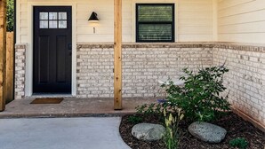 A single-story house with a black front door, a small window with blinds, and a concrete driveway. - Chic studio near ACU (Abilene)