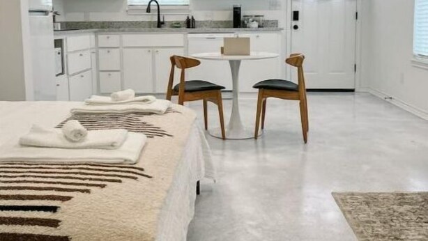 A compact hotel room with a bed, a small dining table, two chairs, a kitchenette, and a door. - Chic studio near ACU (Abilene)