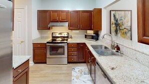 A kitchen with wooden cabinets, stainless steel appliances, granite countertops, and a tiled backsplash.